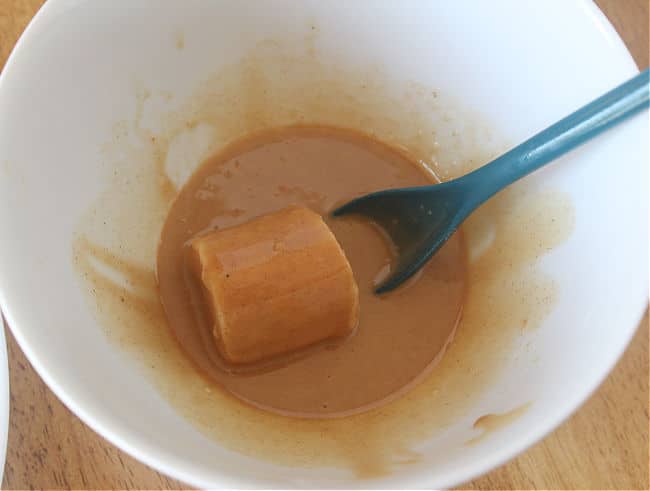 Frozen banana being coated with a peanut butter mixture.