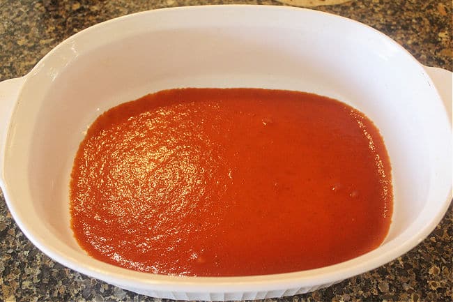 Red sauce spread across the bottom of a baking dish.