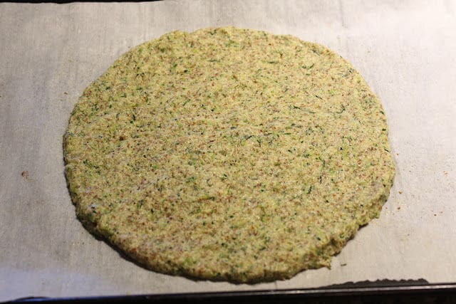 Unbaked zucchini pizza crust on a baking sheet.