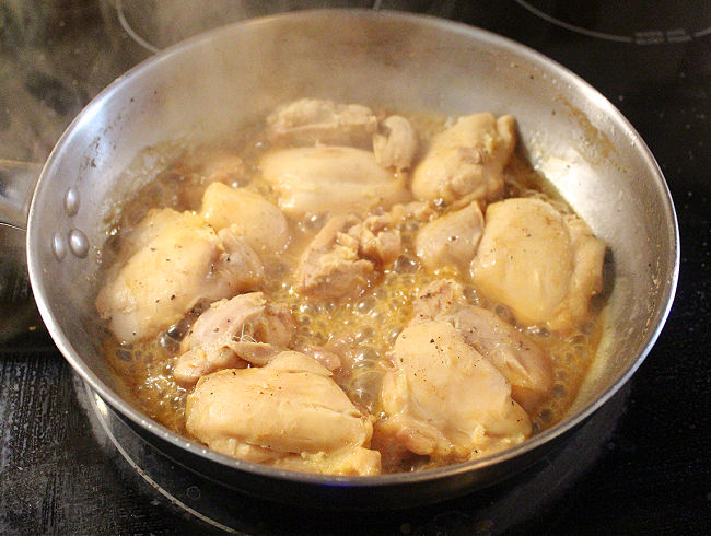 Chicken cooking in apple juice in a pan on the stove.