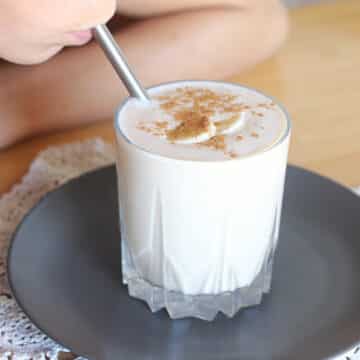 Sipping oat smoothie set on a dark plate.