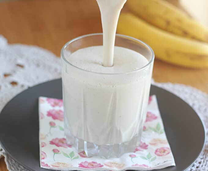 Smoothie being poured into a glass with banana in the background.