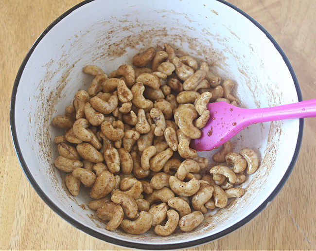 Cashews being stirred in a white bowl.