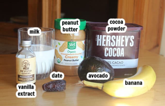 Ingredients on a table, including cocoa, peanut butter, milk, and banana.