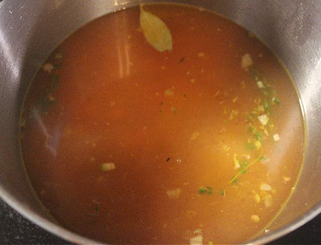 Pot of soup with bay leaf and thyme leaves.