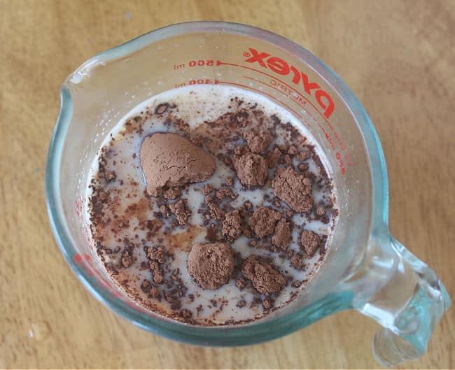 Cocoa powder and milk in a glass measuring pitcher.