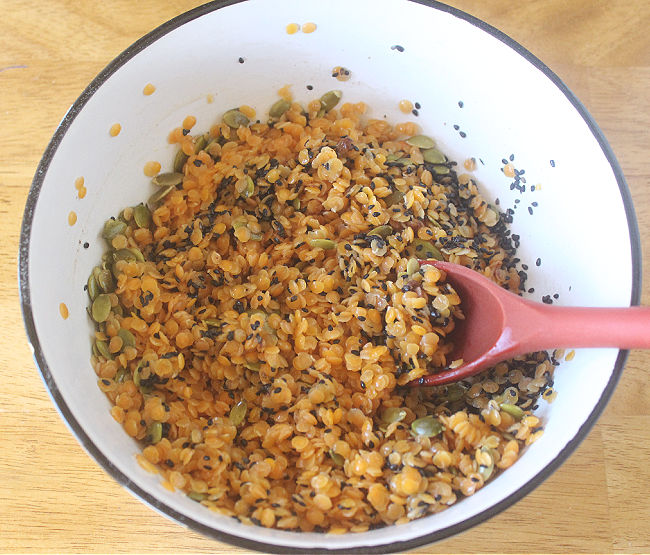 Lentils, pumpkin seeds, and oil being mixed in a bowl.
