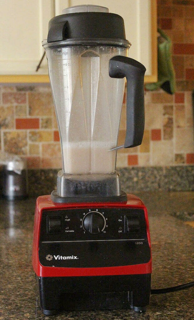 Vitamix blender on a granite counter with milk inside of it.