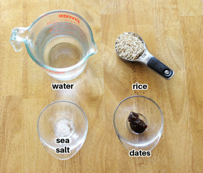 Water, rice, sea salt, and a date in little clear bowls on a wood table.