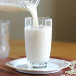 Milk being poured into a glass on a white plate.