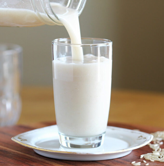 Milk being poured into a glass on a white plate.