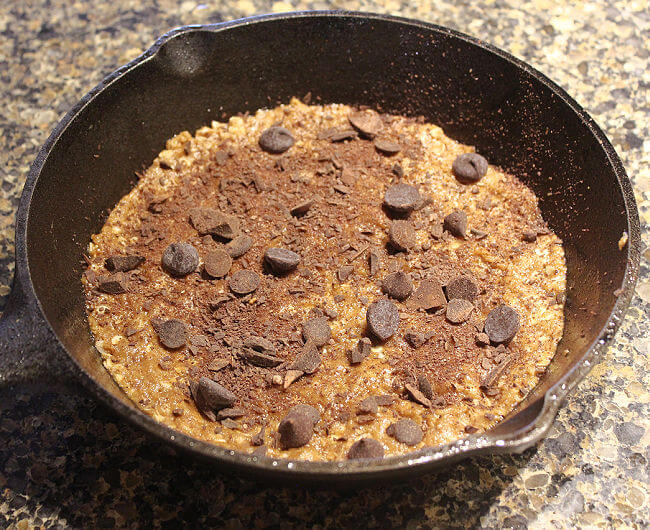Cookie dough with chocolate chips on top in a cast iron skillet.