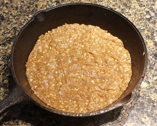 Dough pressed into a small cast iron skillet on a granite countertop.