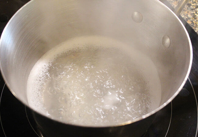 Pot of rice and water boiling in a stainless steel saucepan.