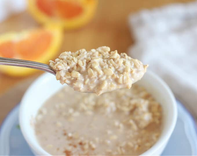 Spoonful of oatmeal with an orange in the background.