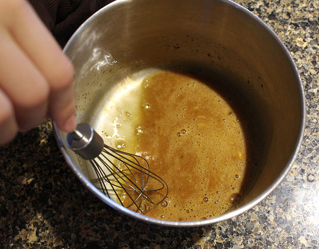 Brown liquid being whisked together in saucepan.