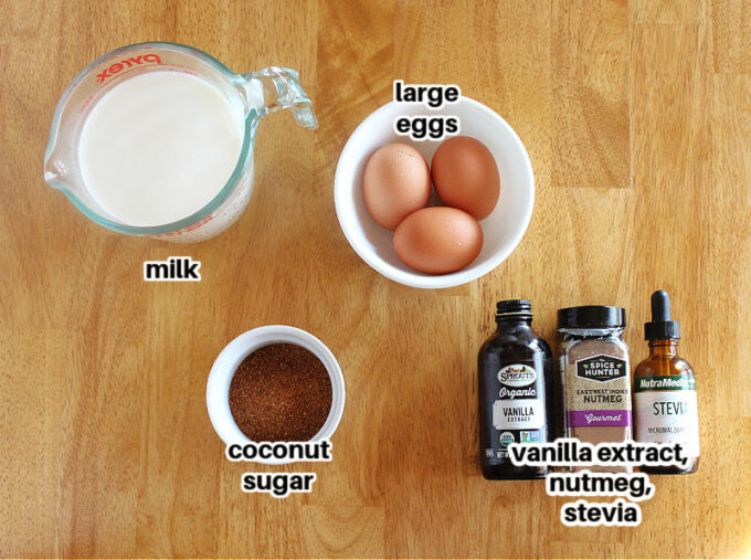 Milk, eggs, sugar, and spices laid out on a wood table.