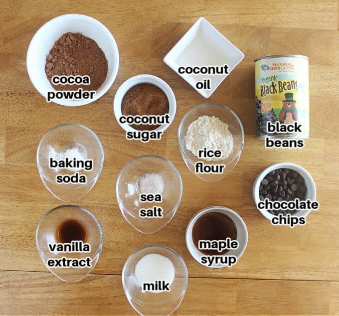 Various ingredients laid out on a wood table, including beans, cocoa, and sugar.