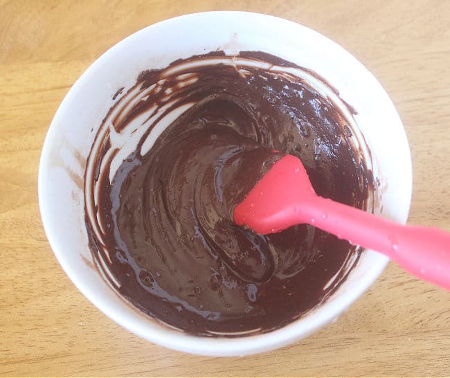 Chocolate ganache in a white bowl with a red spatula.