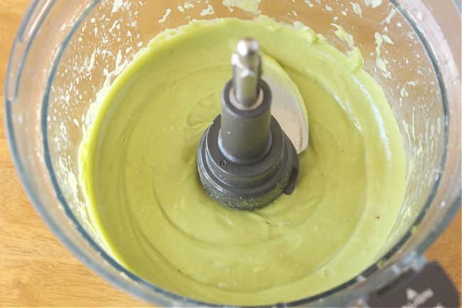 Avocados and other ingredients being mixed in a food processor.