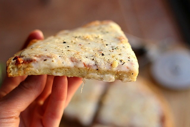 Hand holding a slice of pizza made with quinoa.