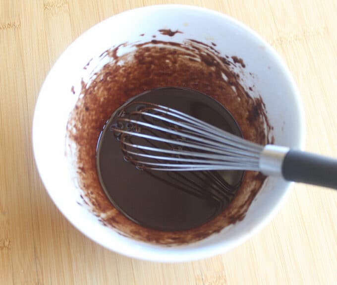 White bowl of dark brown liquid with a whisk in it.