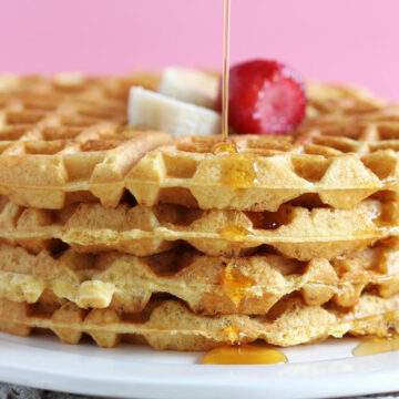 Stack of four waffles topped with strawberry, banana, and syrup.