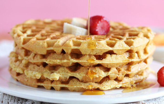 Stack of four waffles topped with strawberry, banana, and syrup.