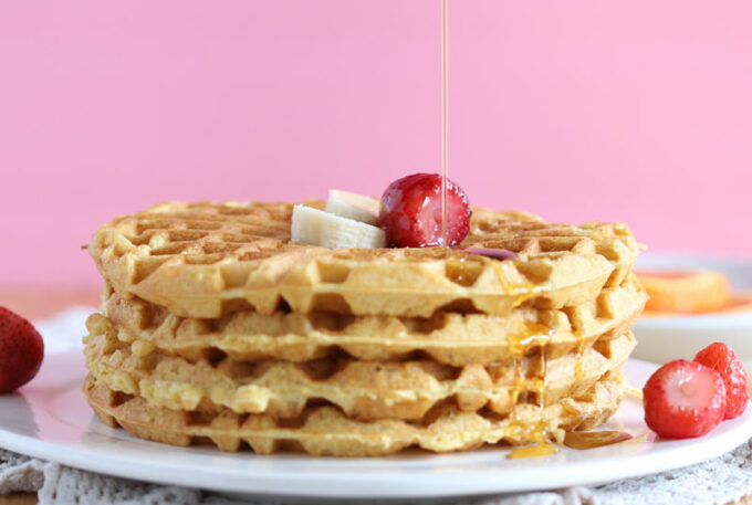 Stack of waffles on a white plate with a pink background.