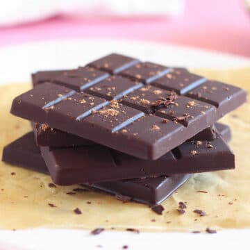 Stack of four chocolate bars with chocolate pieces sprinkled around.