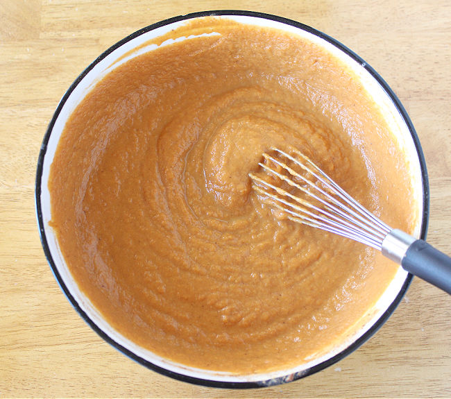 Whisking pumpkin pie filling in a white bowl.