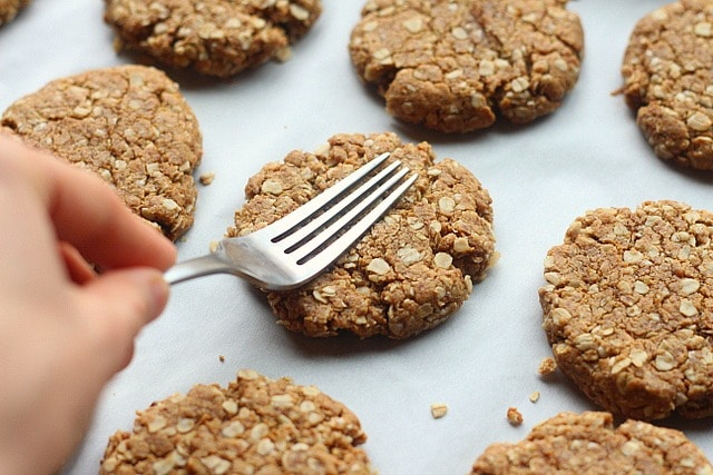 Fork pressing down on a cookie that's on a baking sheet.