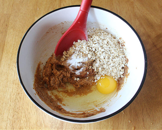 Peanut butter, oats, egg, and baking soda in a large white bowl.