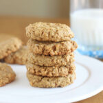 Stack of cookies on a white plate with a glass of milk in the background.