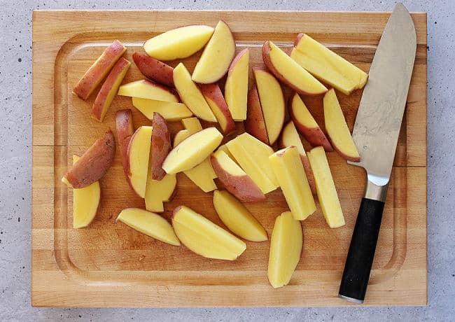 Raw potato wedges on a cutting board.
