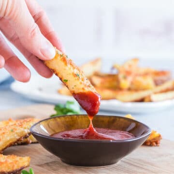 Hand dipping a roasted potato into ketchup.