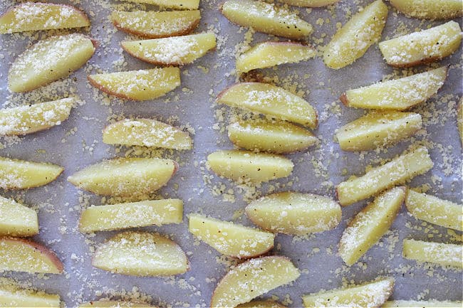 Unbaked parmesan-covered potatoes on a baking sheet.