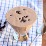 Chocolate protein smoothie with chocolate chips on top in a glass with a spoon.