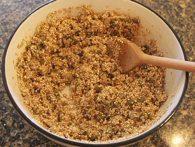 Stirring quinoa with seeds and maple syrup in a white bowl.