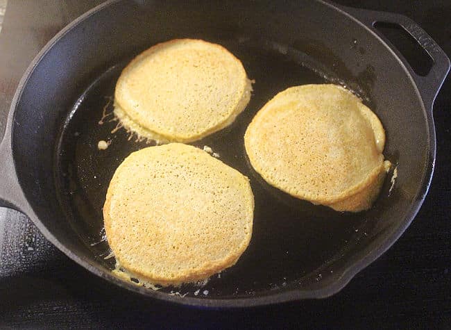 Three cooked pancakes in a cast iron skillet.