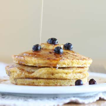 Stack of pancakes with syrup being poured on top.