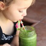 Child drinking green smoothie with a red and white straw.