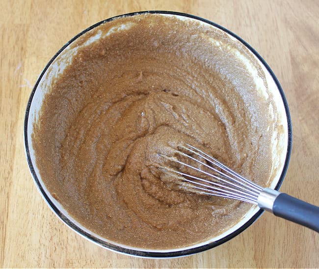 Stirring cake batter with a whisk in a white bowl.