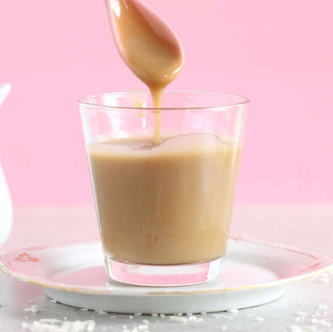 Light brown condensed milk running off of a spoon into a glass.