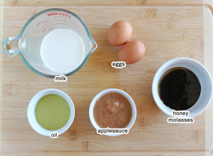 Milk, oil, eggs. applesauce, and molasses on a table.