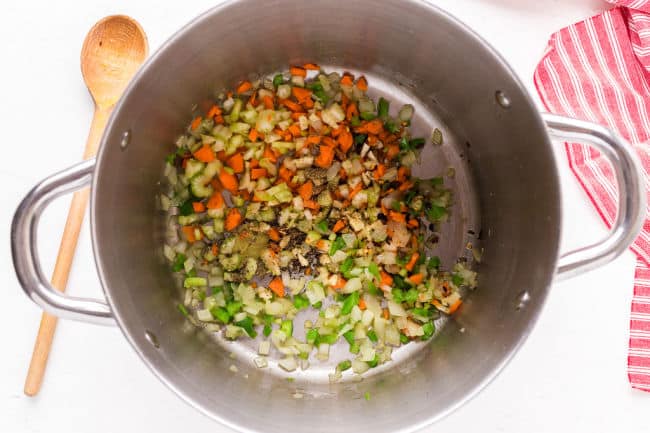 Carrot, onion, celery, and bell pepper cooking in a large pot.