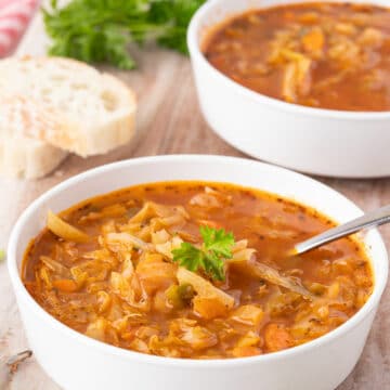 Two bowls of soup laid out on a wood board with bread.