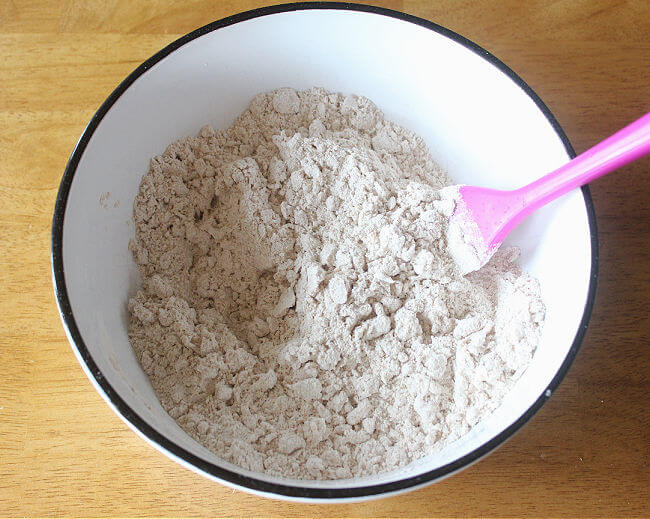 Flour that looks pebbly in a large bowl with a purple spatula.