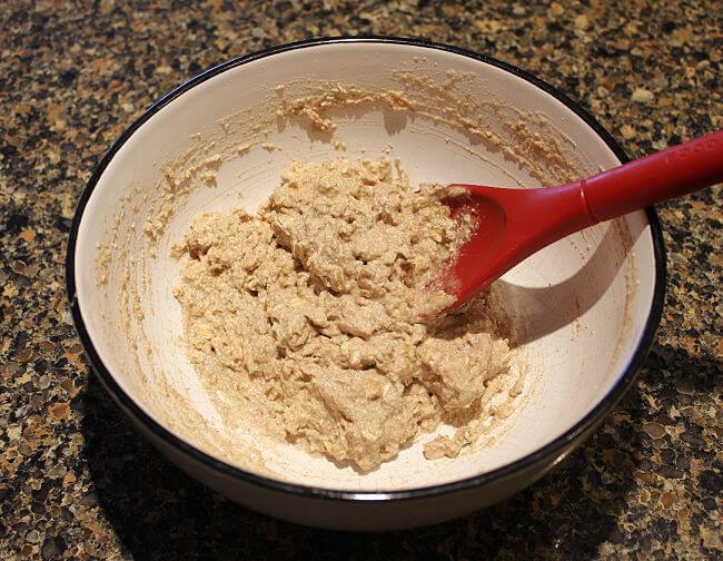 Oatmeal flatbread batter in a large white bowl with a red spoon.