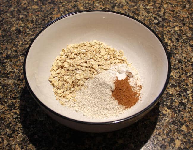 Oatmeal and oat flour in a white bowl on a granite counter.